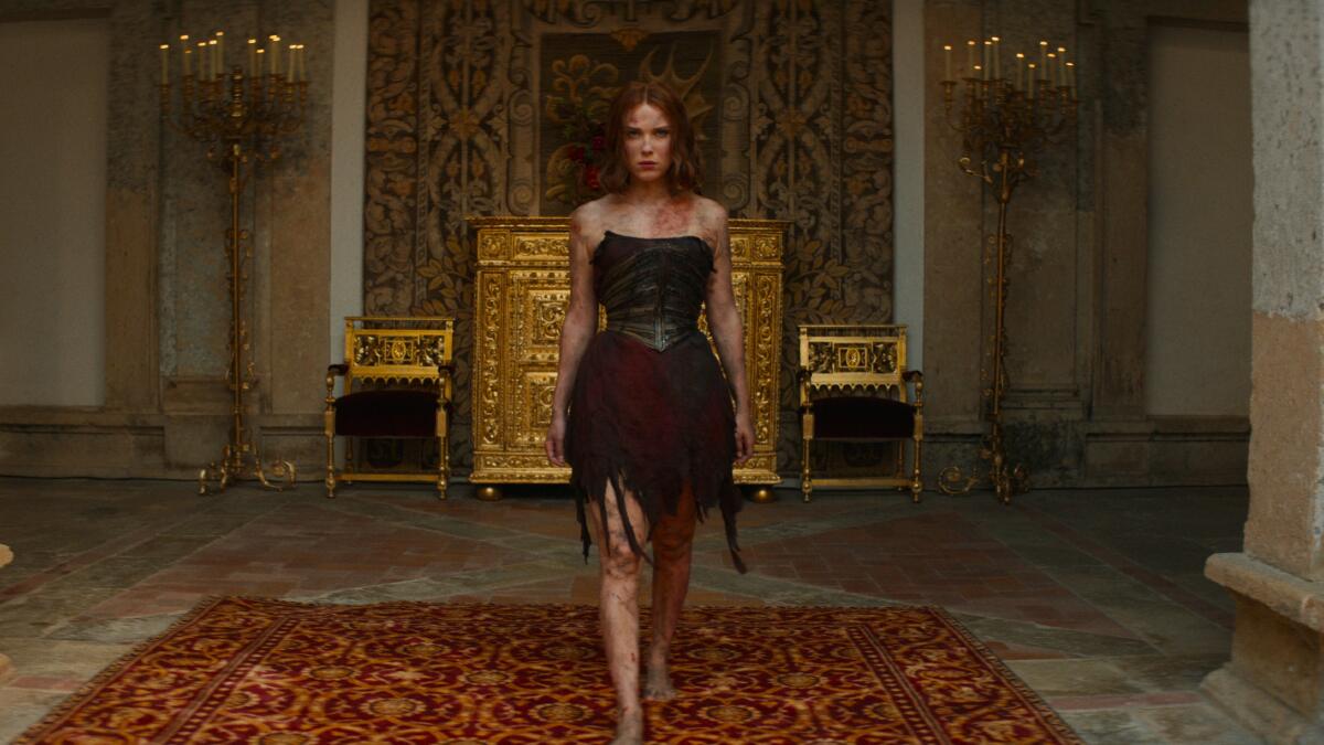Elodie, battered and bruised, walks confidently through a palatial hallway in the movie Damsel.